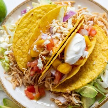 slow cooker chicken tacos in taco shells on plate piled with toppings