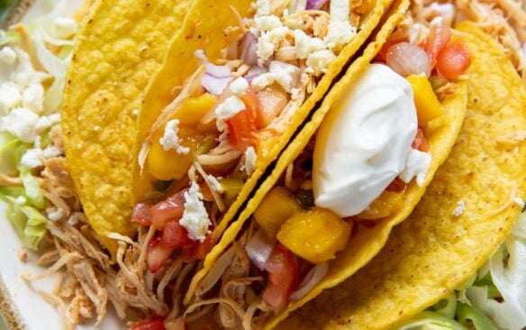 slow cooker chicken tacos in taco shells on plate piled with toppings