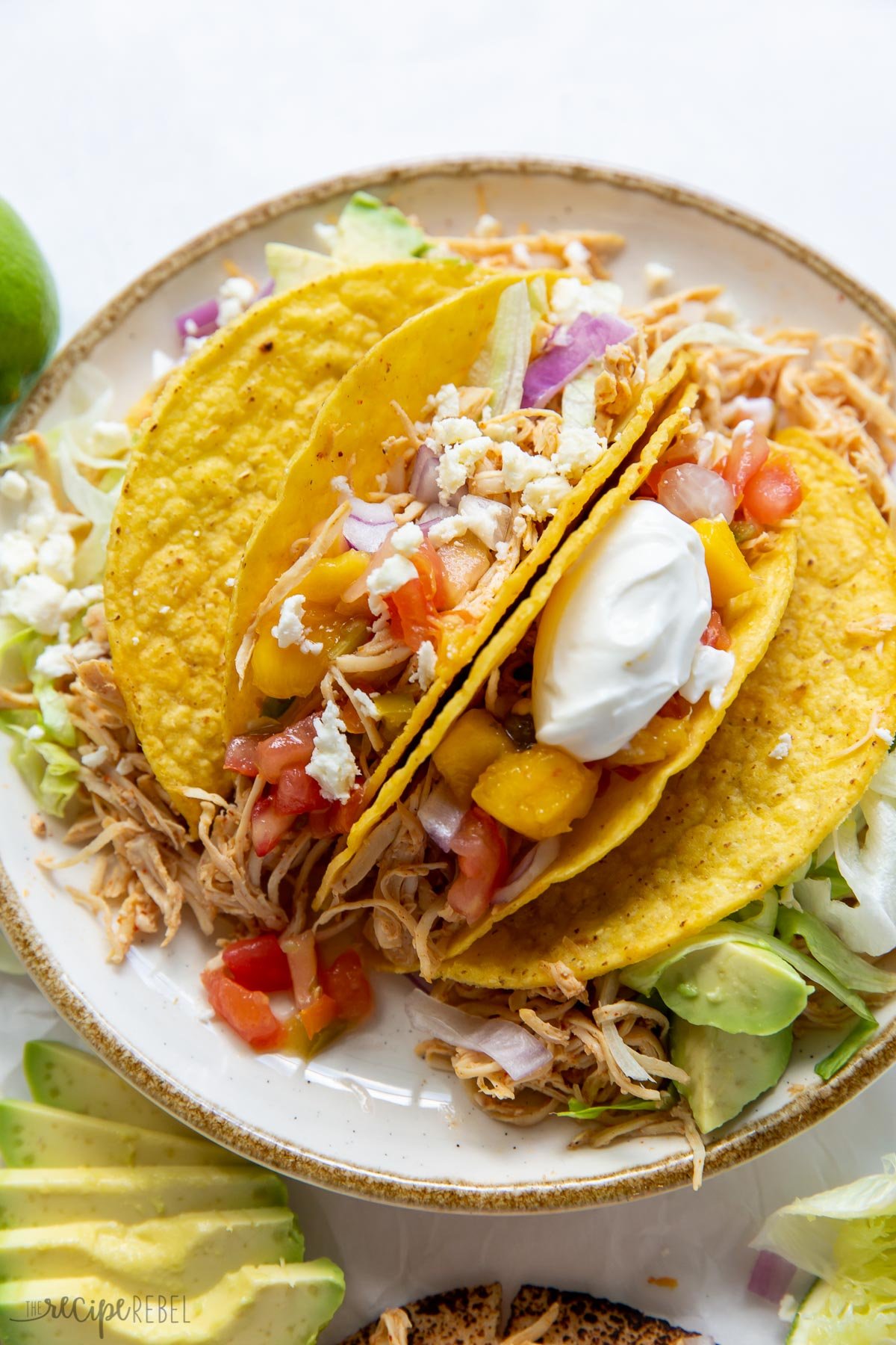 slow cooker chicken tacos in taco shells on plate piled with toppings