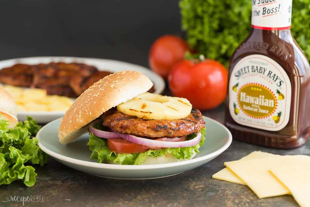 hawaiian chicken burgers on top with sweet baby ray's tomatoes lettuce and cheese slices in the background