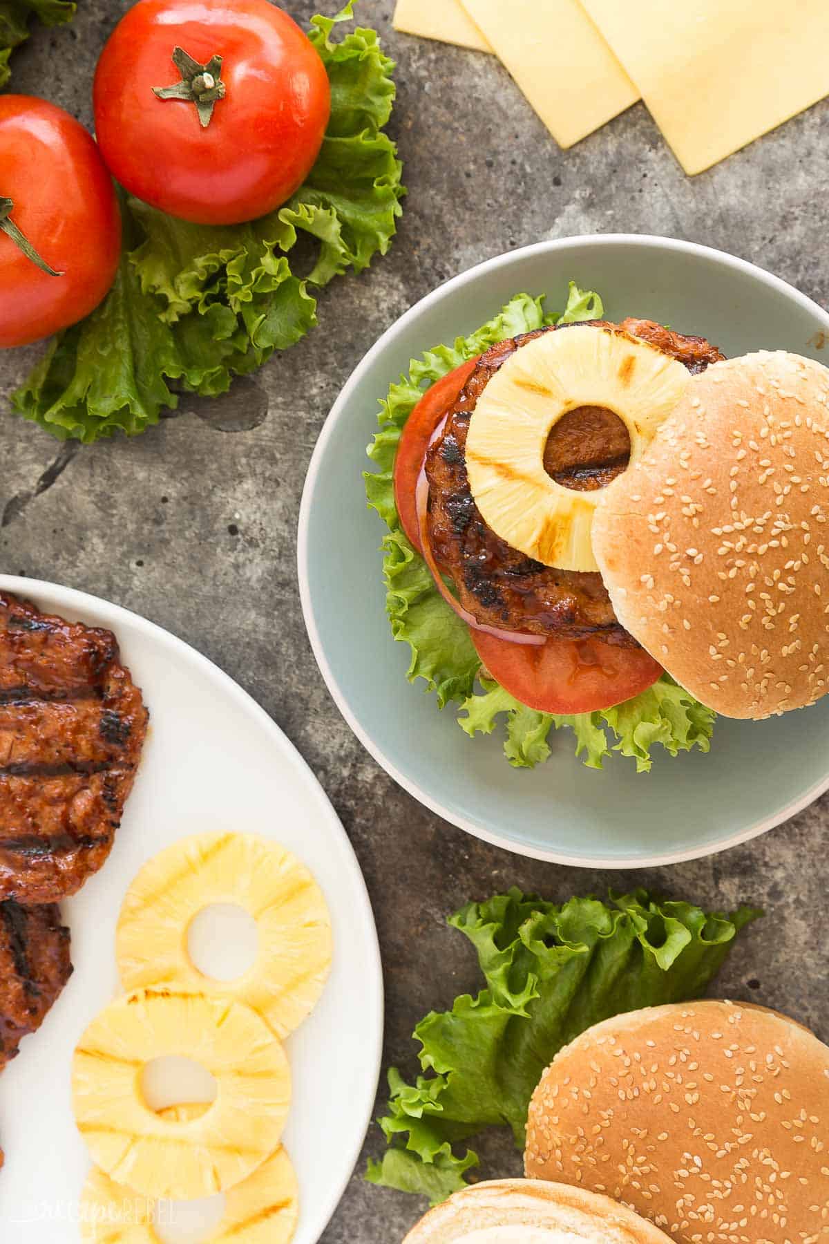 hawaiian chicken burger overhead on bun with pineapple slices and burgers and pineapple slices on white platter