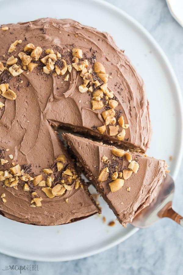 peanut butter cake whole with chocolate frosting and peanuts on top with one slice being removed