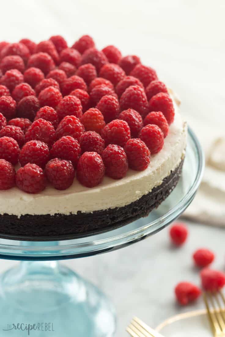 whole brownie bottom cheesecake on blue cake plate topped with fresh raspberries