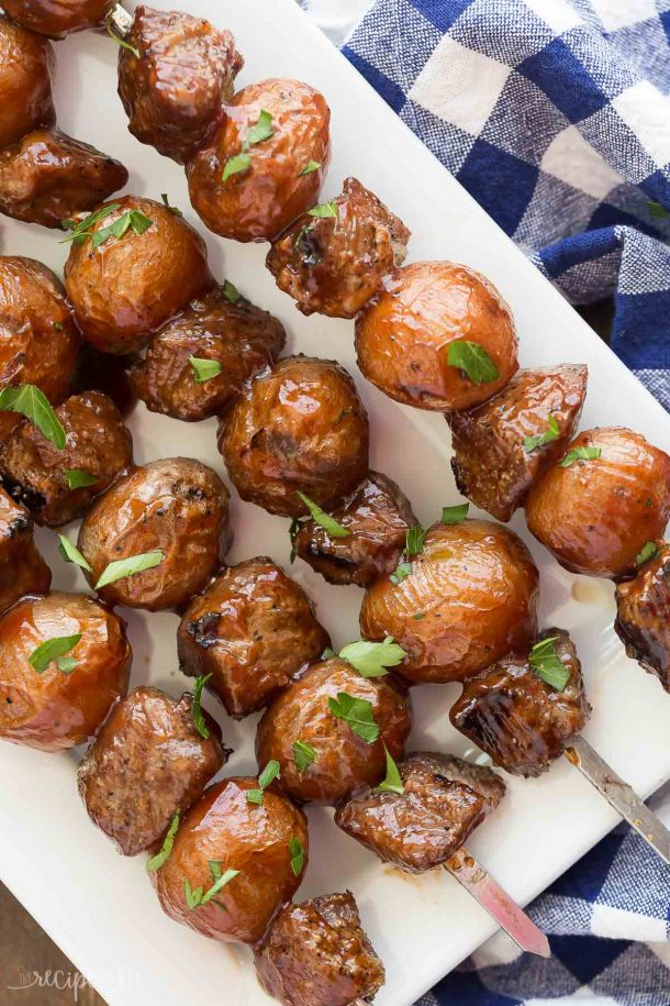 bbq steak and potato skewers overhead on white plate with blue checked napkin on the side