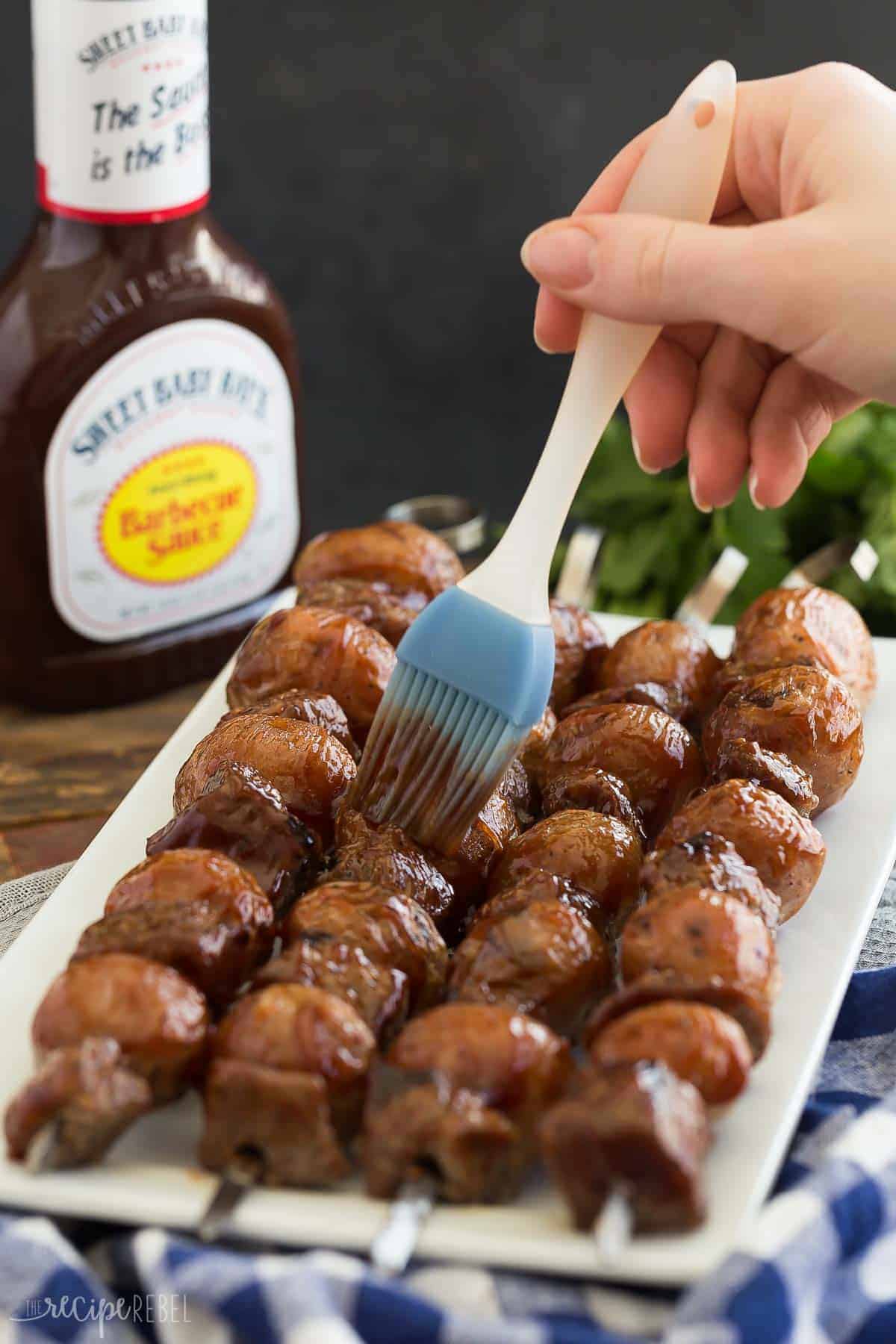 bbq steak and potato skewers on white plate being brushed with sweet baby ray's