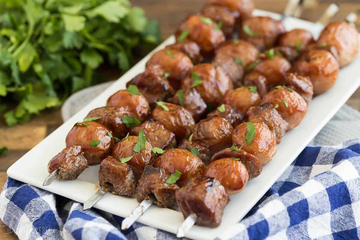 bbq steak and potato skewers on white plate with parsley bunch in the background