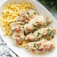 overhead image of creamy italian chicken breasts on a white platter with egg noodles