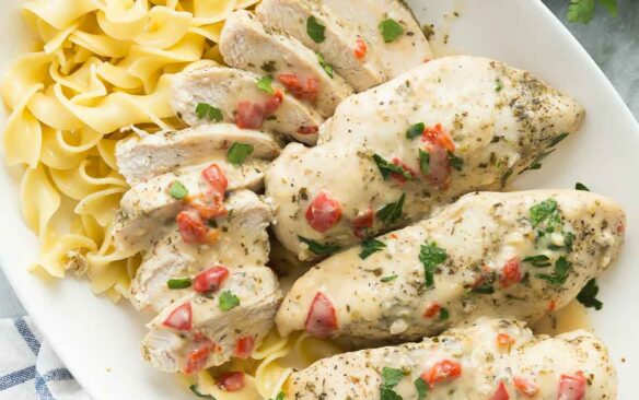 overhead image of creamy italian chicken breasts on a white platter with egg noodles