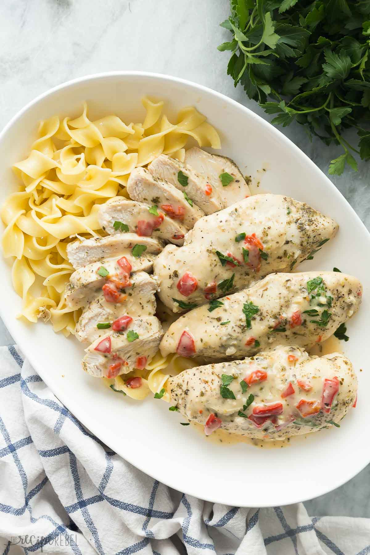 overhead image of creamy italian chicken breasts on a white platter with egg noodles