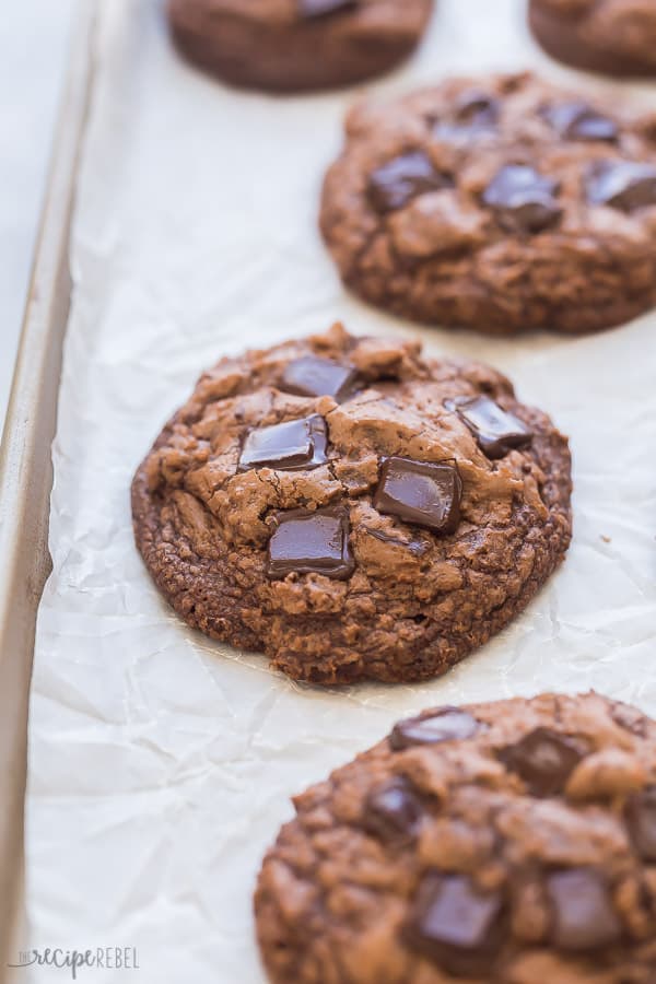 These Double Chocolate Chip Cookies are made with MELTED chocolate which makes them ridiculously fudgy! These are chocolate cookies for chocolate lovers, with crispy edges, and a chewy, fudgy center. #chocolate #cookies #cookierecipe #baking #baking #recipes double chocolate chip cookies on pan lined with parchment paper and melted chocolate chunks