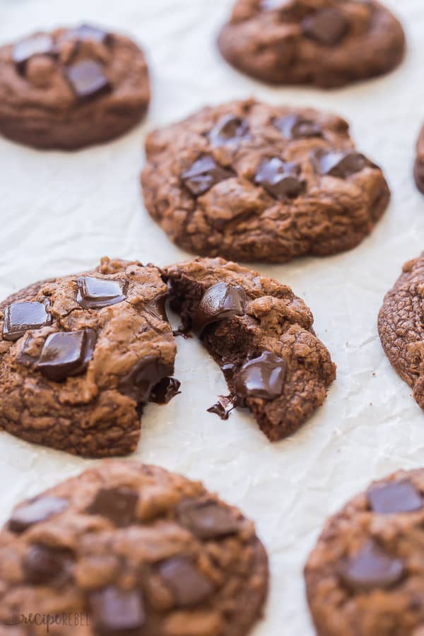 These Double Chocolate Chip Cookies are made with MELTED chocolate which makes them ridiculously fudgy! These are chocolate cookies for chocolate lovers, with crispy edges, and a chewy, fudgy center. #chocolate #cookies #cookierecipe #baking #baking #recipes double chocolate chip cookie close up on baking sheet broken in half