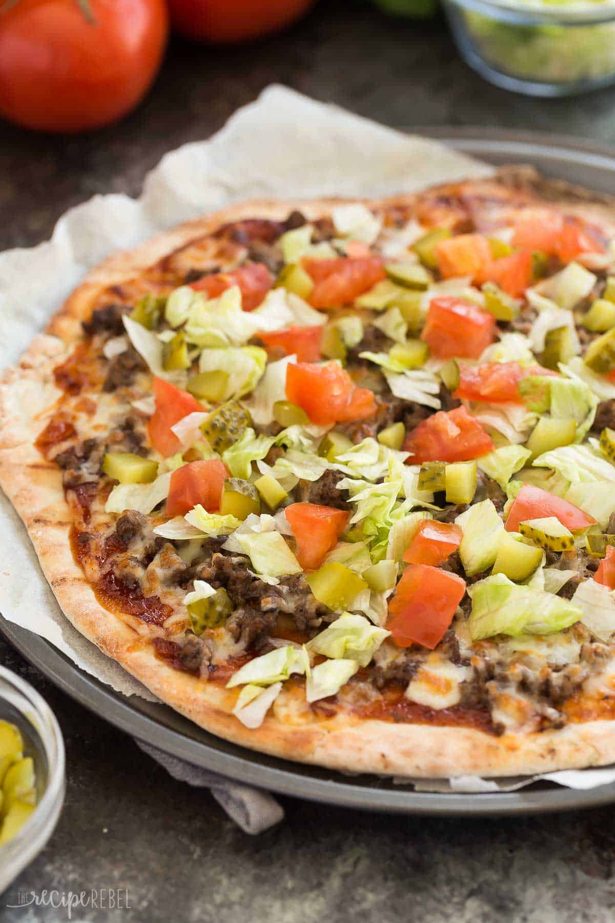 grilled cheeseburger pizza close up with tomatoes lettuce and pickles on top