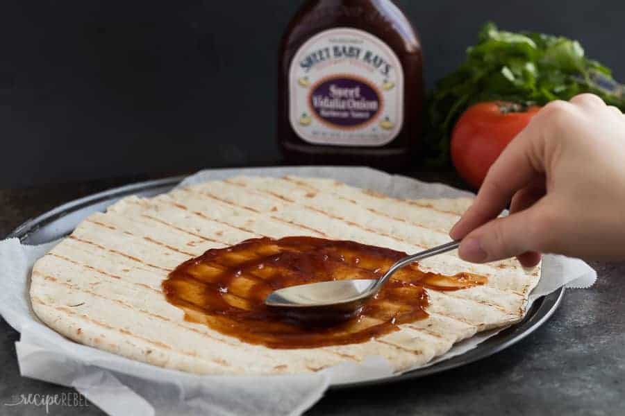grilled pizza crust on parchment lined pizza pan being coated in barbecue sauce