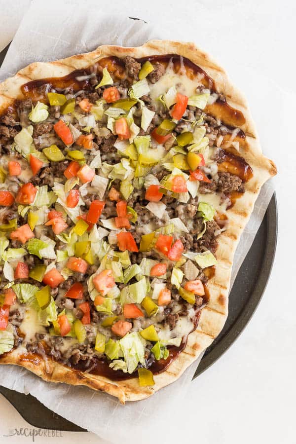 grilled cheeseburger pizza overhead on parchment lined pizza pan on white background