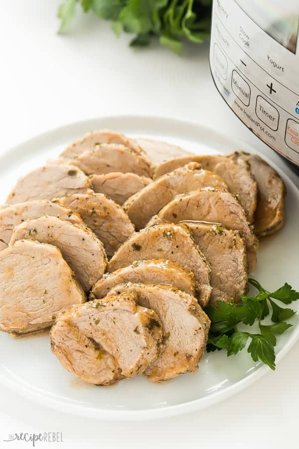 instant pot pork tenderloin on a white plate sliced with pressure cooker in the background