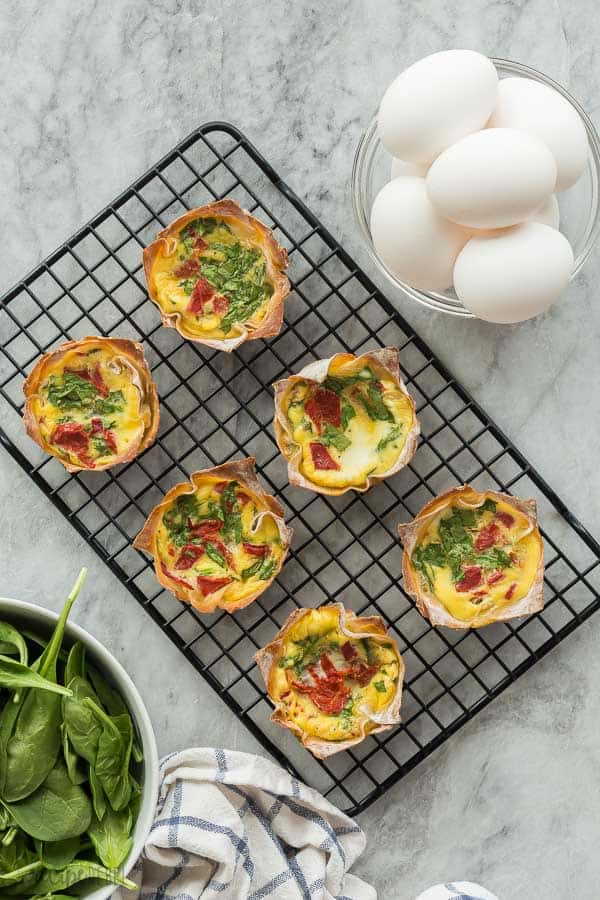 mini quiche recipe on a wire rack with whole eggs and spinach on the side