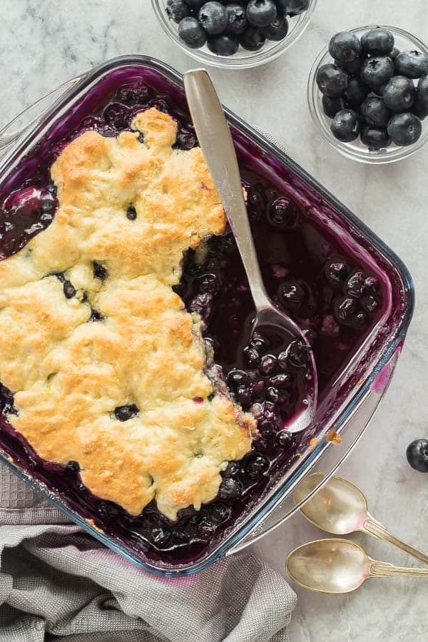 blueberry cobbler in a glass pan overhead with a spoon stuck into pan 