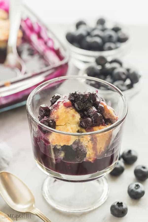 blueberry cobbler in glass bowl with fresh blueberries in the background