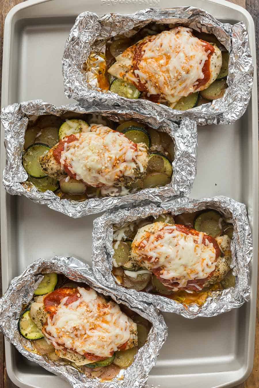 chicken parmesan foil packs with potatoes and zucchini overhead on sheet pan