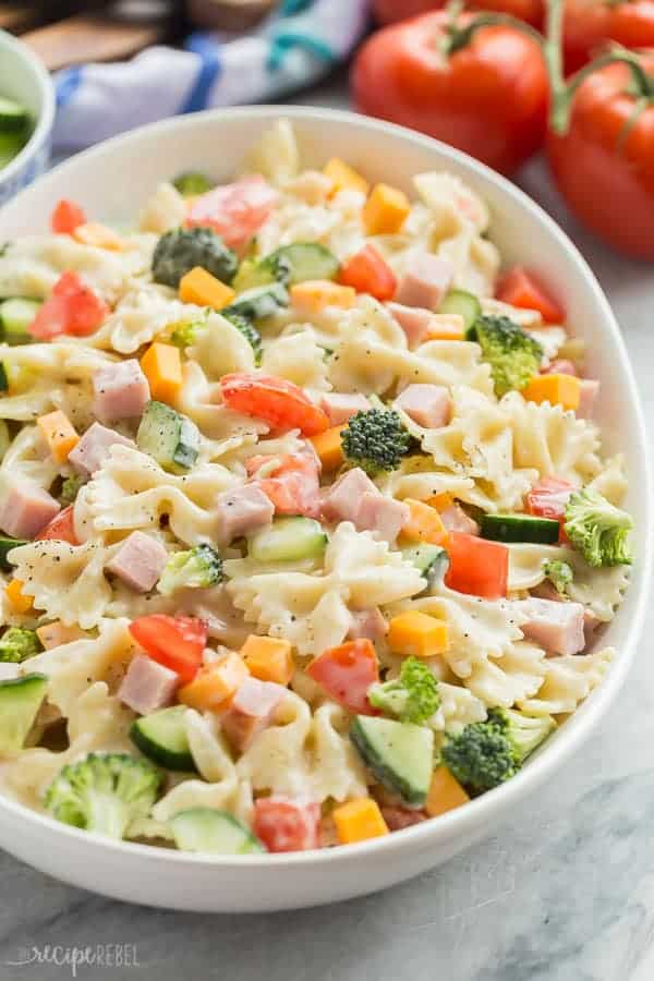 creamy ranch bowtie pasta salad in a large white bowl with tomatoes in the background
