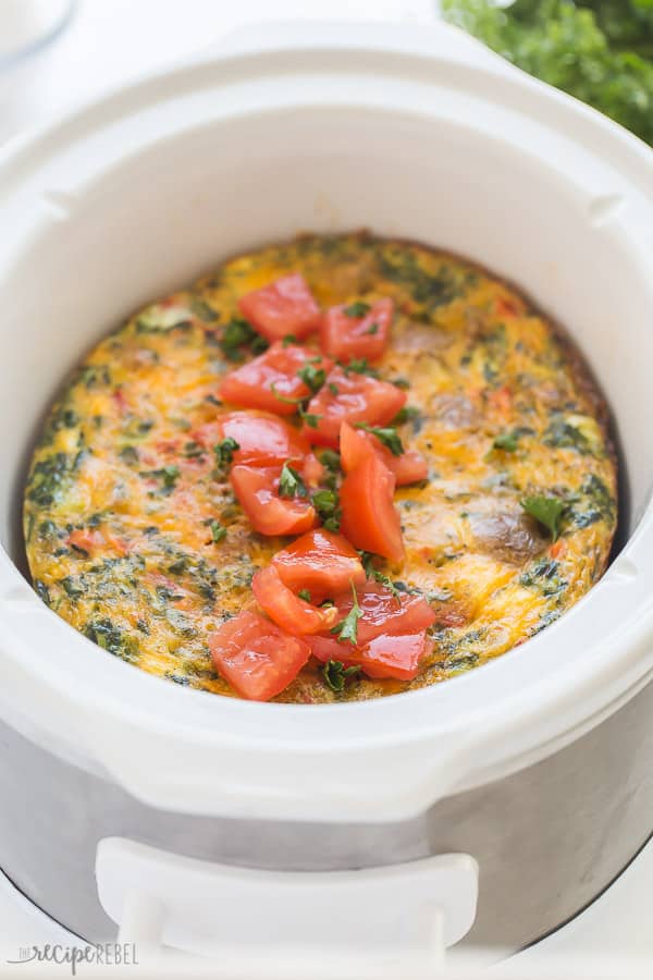 crockpot breakfast casserole in white slow cooker with fresh tomato chunks on top