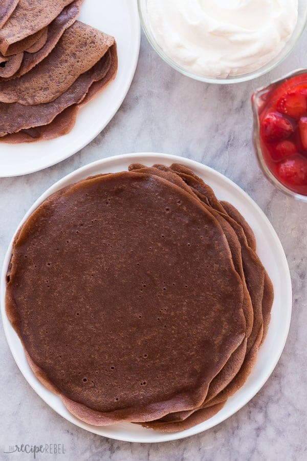 These Easy Chocolate Crepes are a simple but decadent breakfast, brunch or dessert recipe! Fill them any way you want -- with whipped cream, cream cheese, or fresh fruit, this is an easy crepe recipe to make ahead for a special occasion. #chocolate #crepes #breakfast #brunch #dessert chocolate crepes on white plate overhead on grey marble background