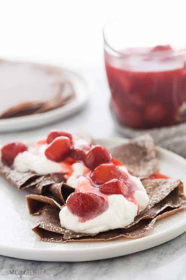 chocolate crepes on white plate with whipped cream and strawberry sauce