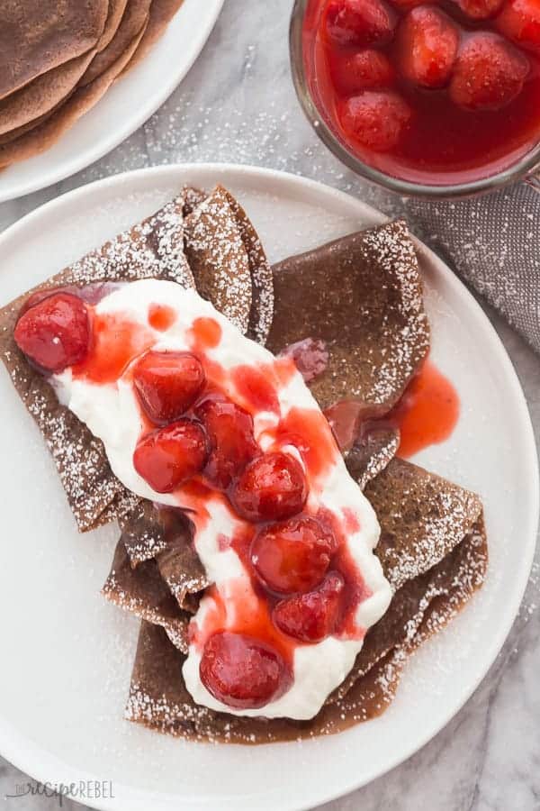 chocolate crepes with whipped cream and strawberry sauce overhead on white plate