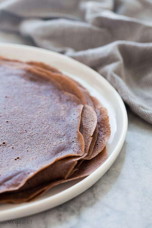 chocolate crepes stack on white plate with grey towel in the background