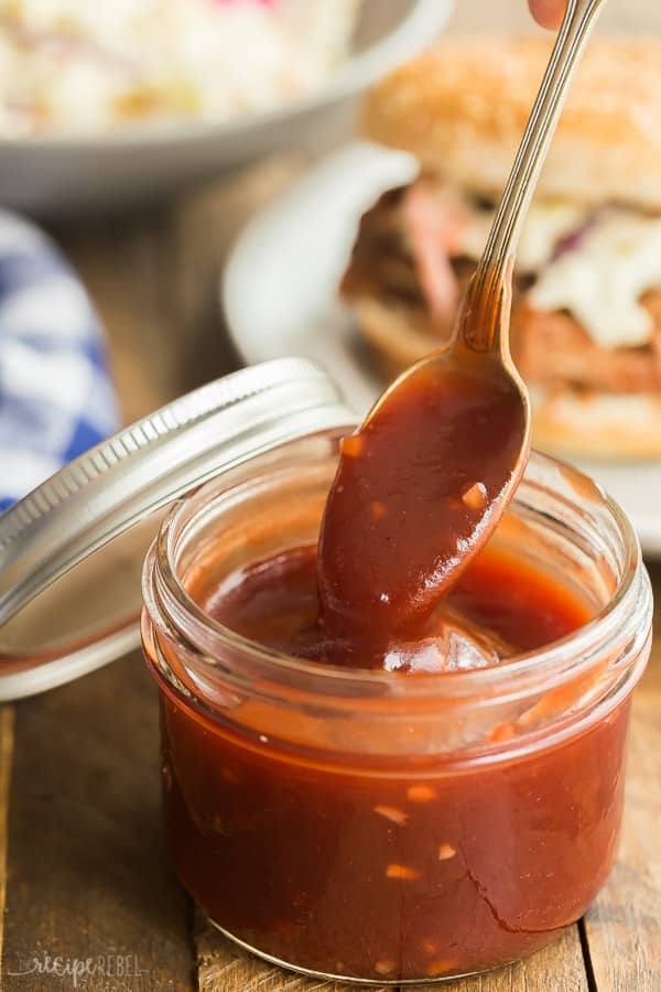cranberry barbecue sauce in a clear jar with spoon scooping some up