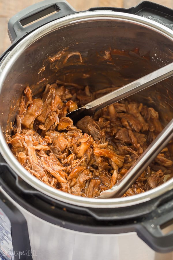 pulled pork with cranberry bbq sauce in the pressure cooker with metal tongs stuck in