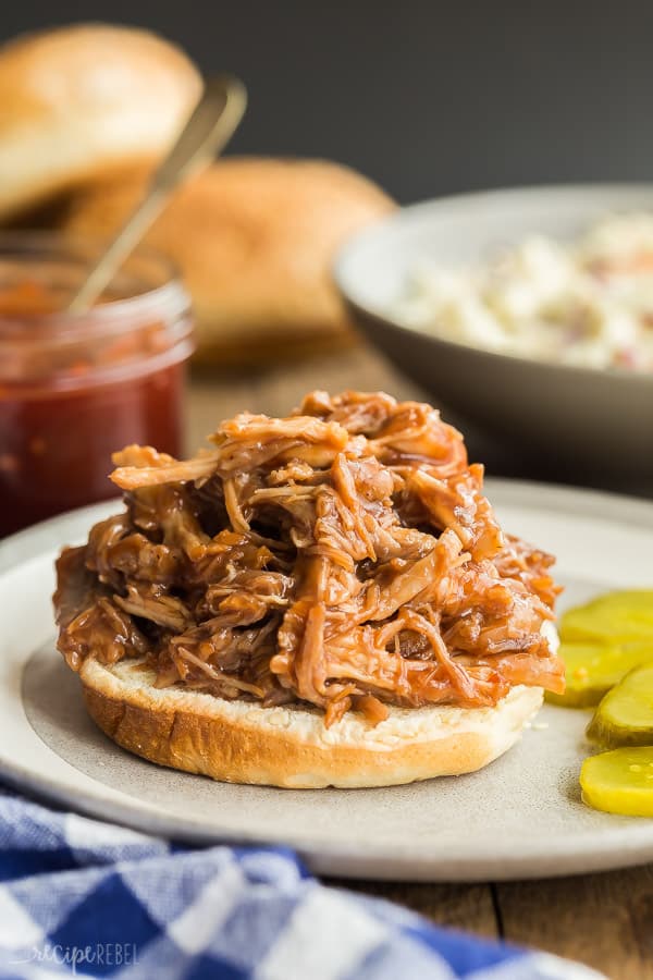 instant pot pulled pork on a bottom bun on a plate with pickles on the side