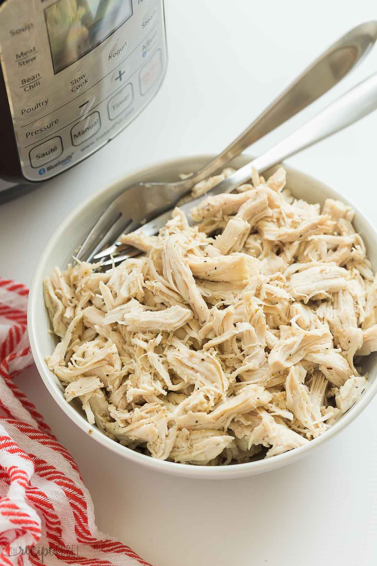 instant pot shredded chicken in bowl with two forks and instant pot in the background.