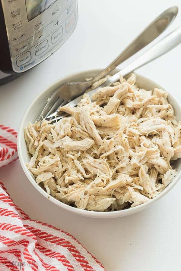 instant pot shredded chicken in bowl with two forks in bowl and pressure cooker in the background