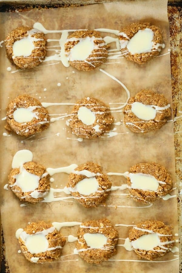 no bake lemon thumbprint cookies on piece of parchment paper with glaze drizzle over top