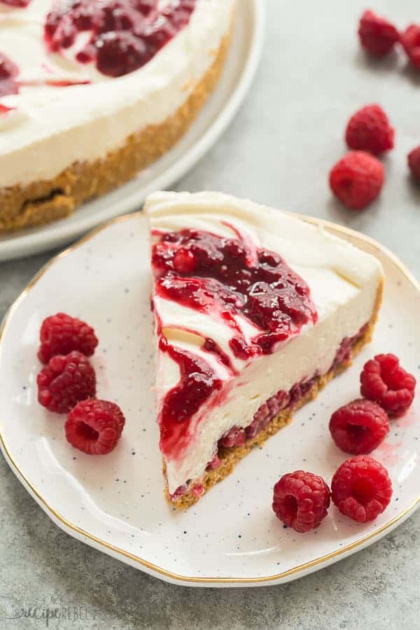white chocolate raspberry cheesecake slice on white plate with whole cheesecake in background