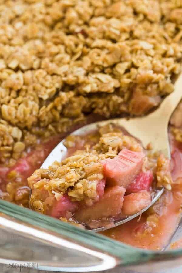 close up image of rhubarb crisp on a metal serving spoon in a glass pan