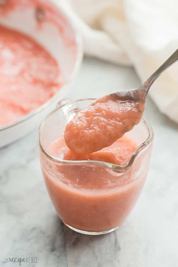 pink rhubarb sauce in a glass cup with spoon scooping up some sauce