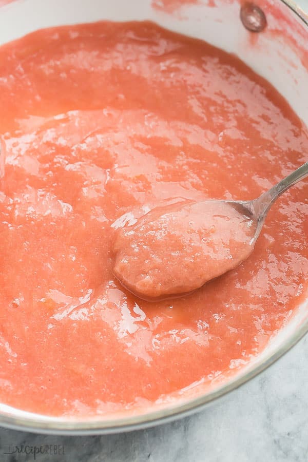 pink rhubarb sauce in white pan with spoon stuck in sauce