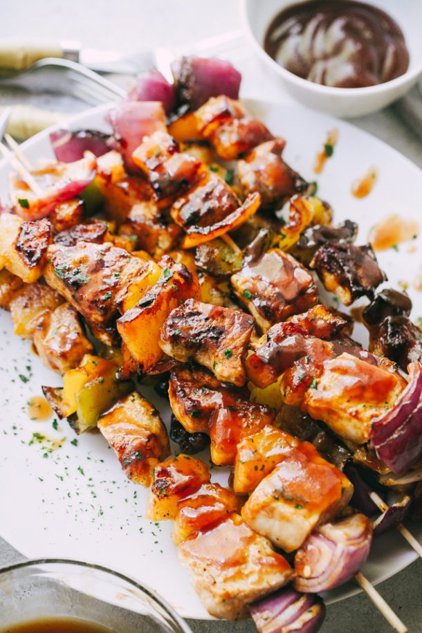 barbecue pineapple and pork skewers on white plate with barbecue sauce in the background