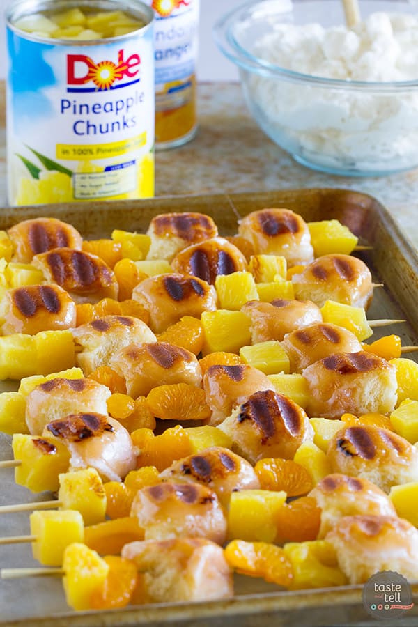 grilled donut and fruit kabobs on a sheet pan with cans of pineapple in the background