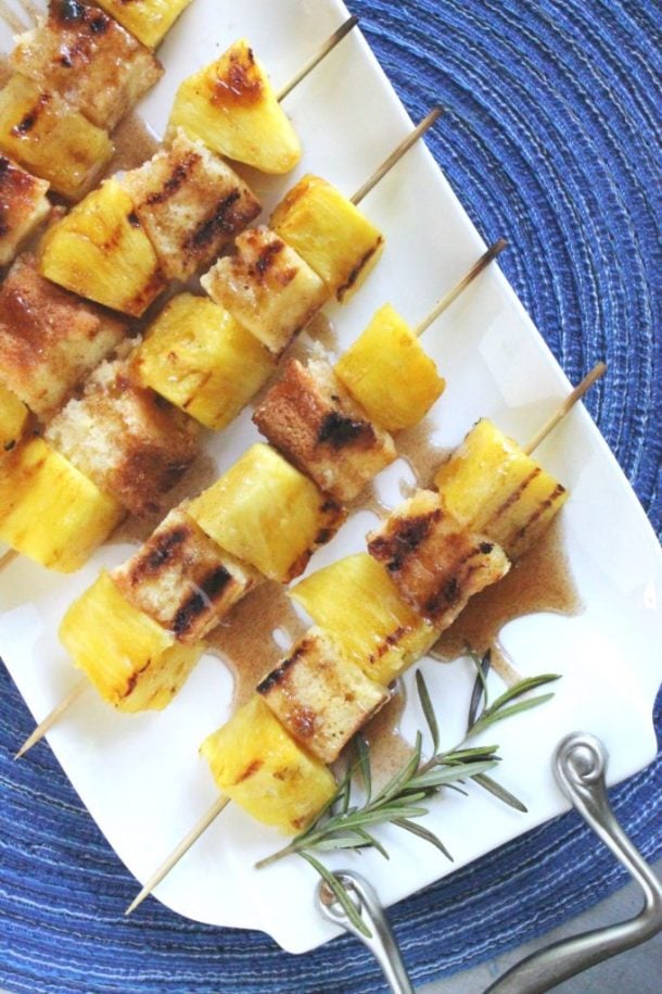 grilled pineapple pound cake kabobs on white plate on top of blue background