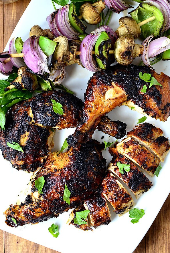 root beer can chicken grilled and sitting on a white plate with grilled vegetables