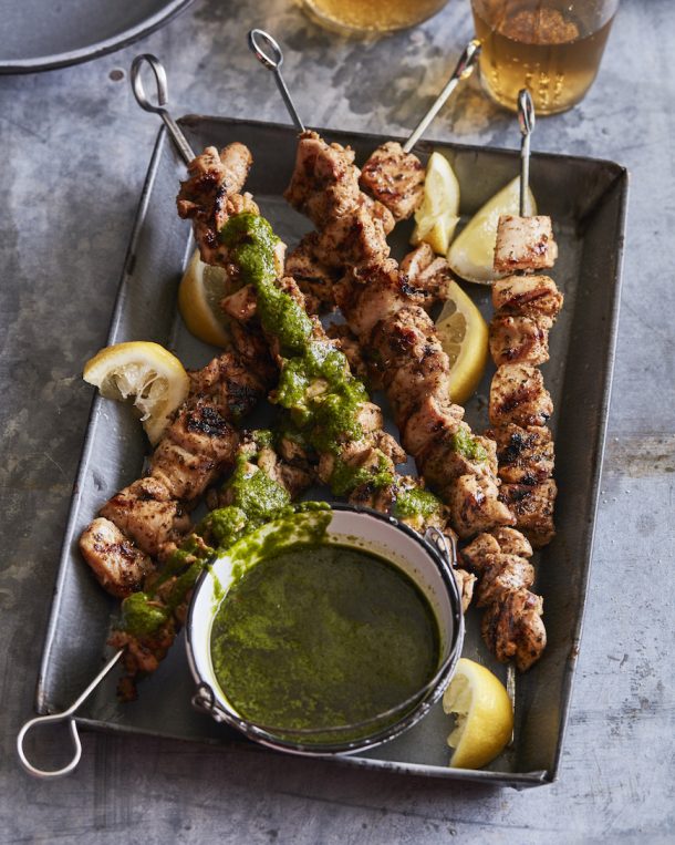 chicken shish kabobs on metal skewers on a grey metal plate with lemon wedges on the side