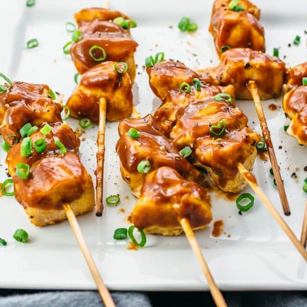 grilled chicken satay on wooden skewers resting on white plate and sprinkled with green onions