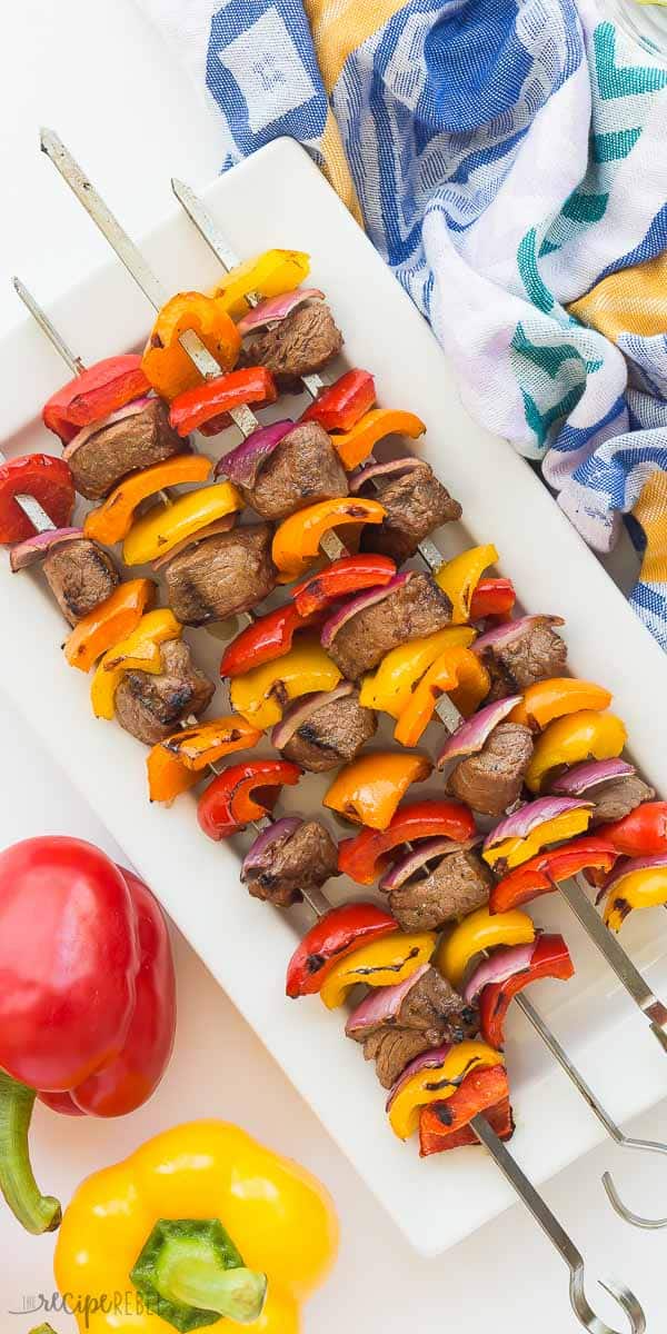 fajita steak kabobs on a white plate with blue towel and whole peppers on the side