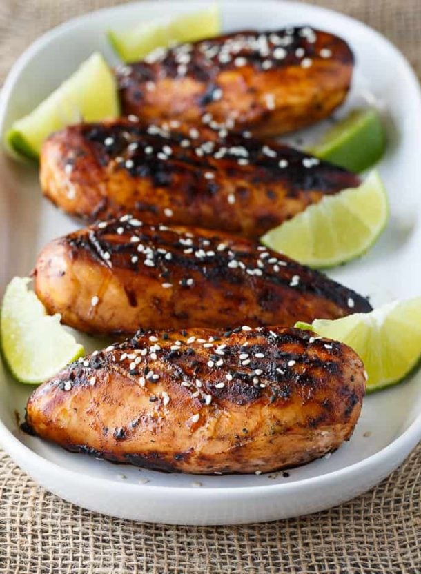 honey sriracha chicken breasts with sesame seeds on top and lime wedges all around