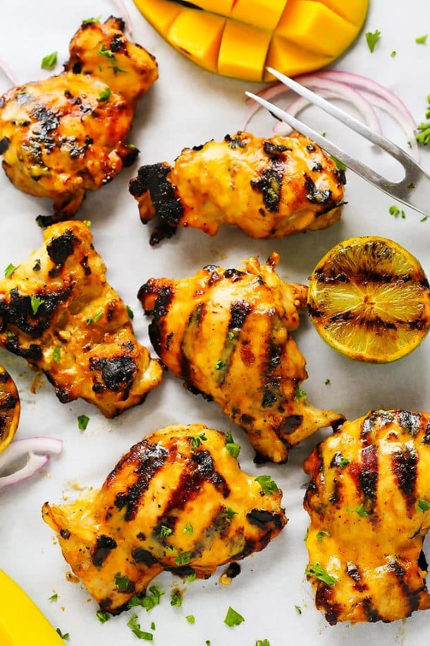 mango lime grilled chicken thighs with grilled lemon halves and fresh mango on the side