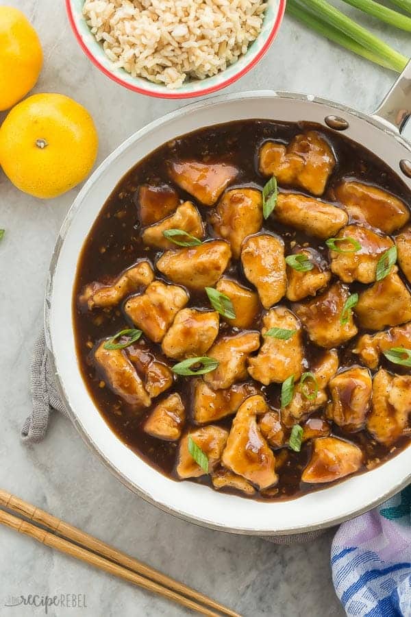 orange chicken in pan overhead on grey marble background with oranges on the side