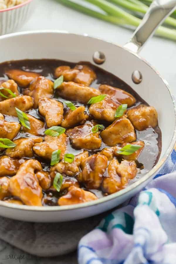 orange chicken in white skillet with green onions on top and blue towel on the side